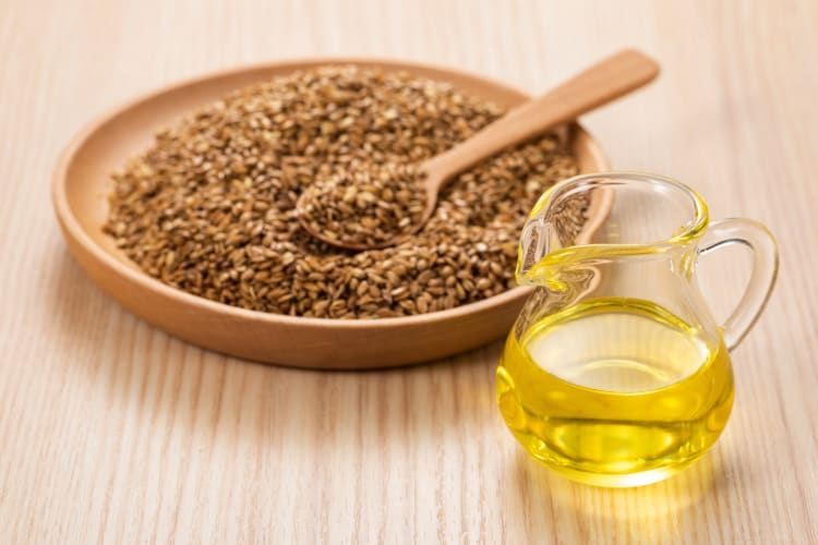 A glass jug of oil next to a plate of flaxseeds