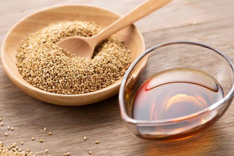 Sesame seeds in a bowl next to sesame oil