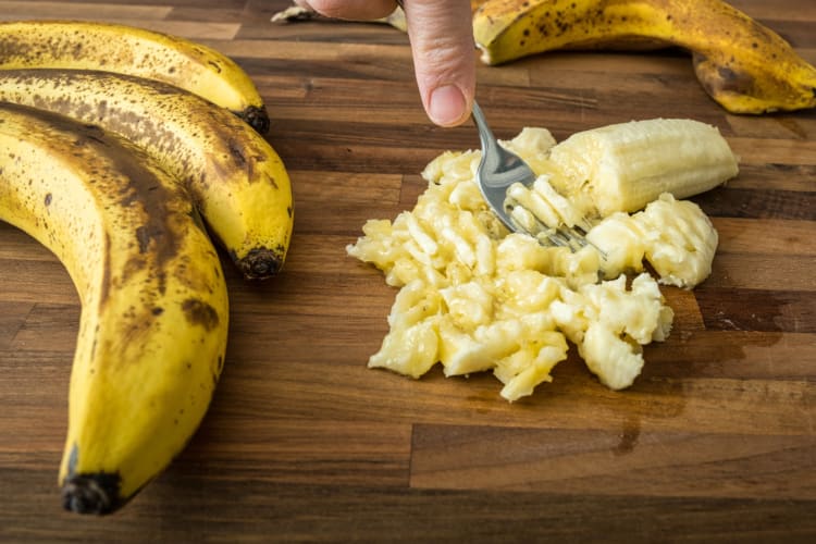 A person mashing banana with a fork next to whole bananas