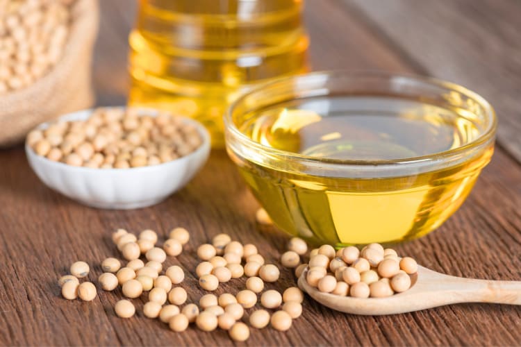 A glass bowl with soybean oil next to soy beans