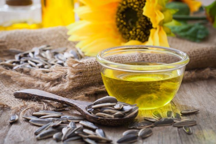 A bowl of sunflower oil next to sunflower seeds and flowers