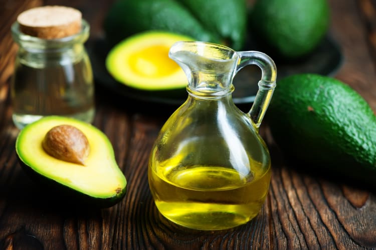 A small glass jar of avocado oil next to fresh avocados
