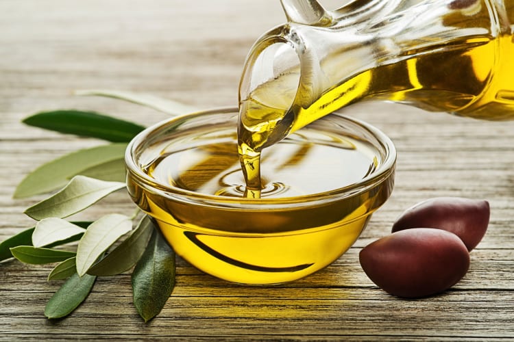 Olive oil being poured from a glass container into a glass bowl