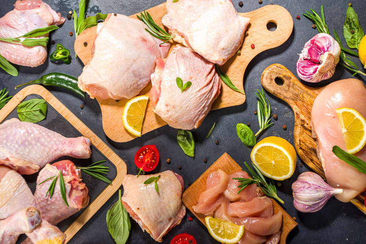 Variety of uncooked cuts of chicken on chopping boards with garnish all around them