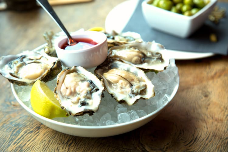 Wood fired oysters in a bowl over ice with sauce in the middle