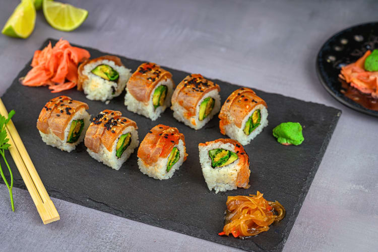 Eight pieces of sushi served on a board with chopsticks, ginger and wasabi