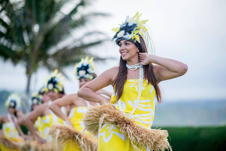 One woman in the foreground with others in the background, all performing an Hawaiian dance