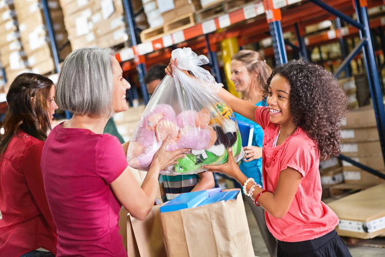 A young girl donating a bag of toys to volunteers for a toy drive
