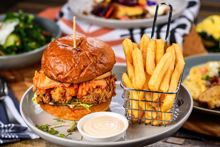 Chicken burger next to fries in a metal serving tray, served with sauce on the side