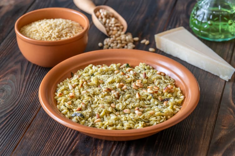 A bowl of orzo pasta and pine nuts next to uncooked orzo and Parmesan cheese 