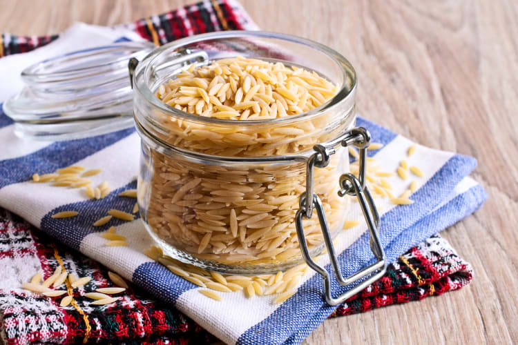 A glass jar with orzo pasta on top of cloths