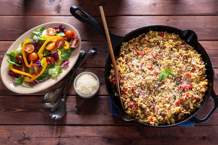 An orzo dish in a cast iron pan next to a salad 