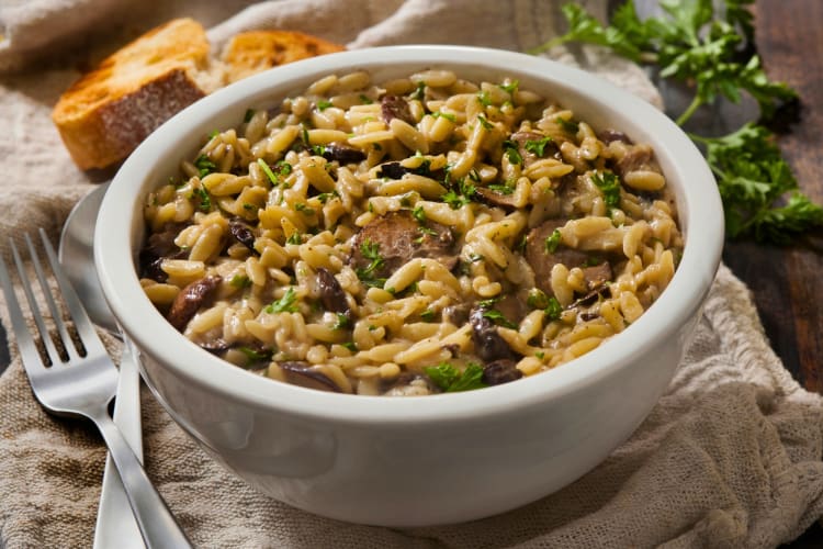 A bowl of mushroom orzo with bread in the background