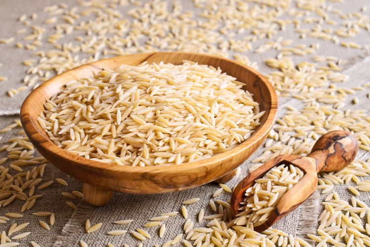 Dried orzo in a wooden bowl and wooden spoon