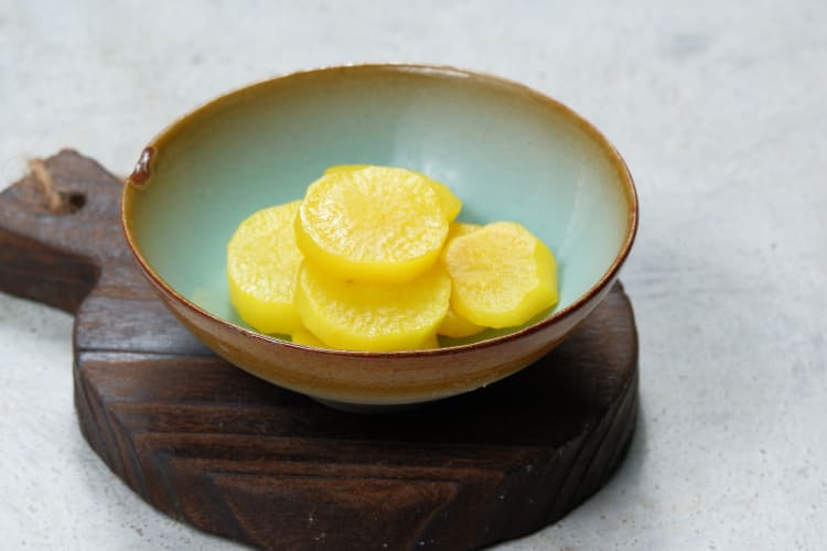 Sticks of yellow oshinko in a bowl on a bamboo sushi mat