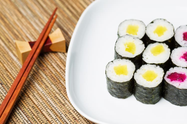 Maki sushi rolls with yellow and purple filling on a plate next to chopsticks