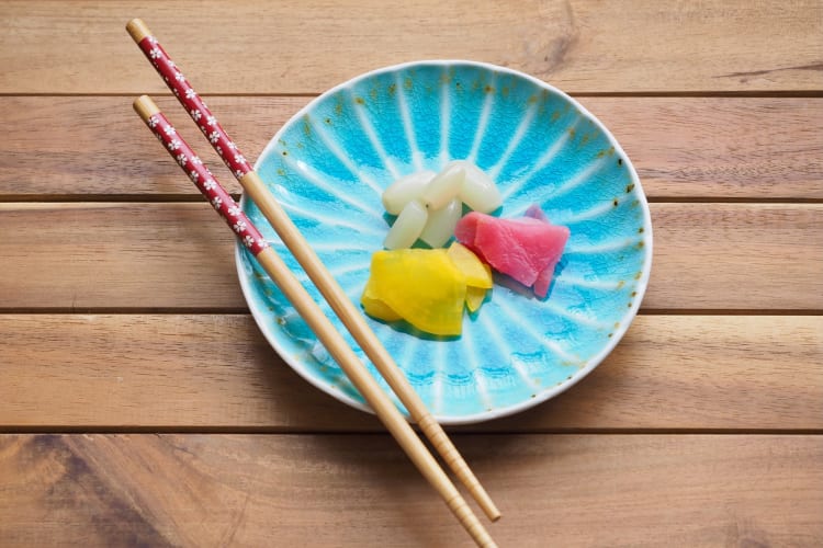 Three kinds of Japanese pickles on a blue plate next to chopsticks