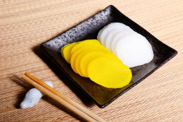 Yellow and white oshinko on a plate next to chopsticks on a chopstick holder