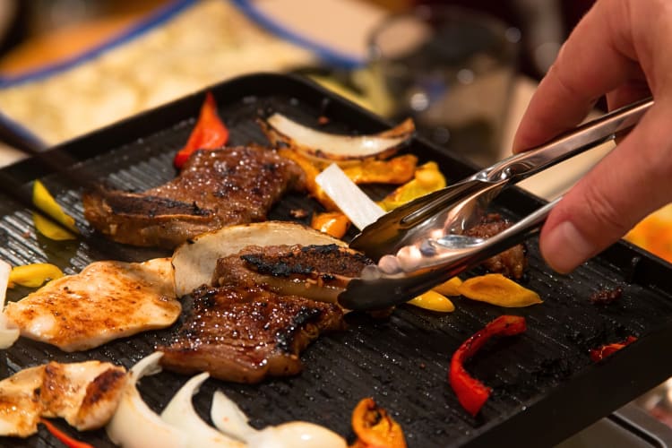 Person using tongs to flip food on an electric hibachi