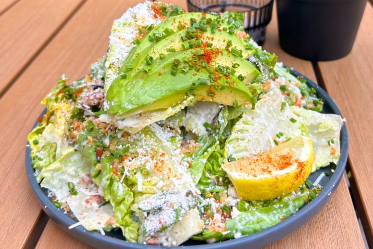 A Caesar salad with avocado on a wooden outdoor table