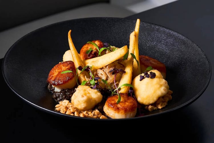 A seared scallop dish on a black plate