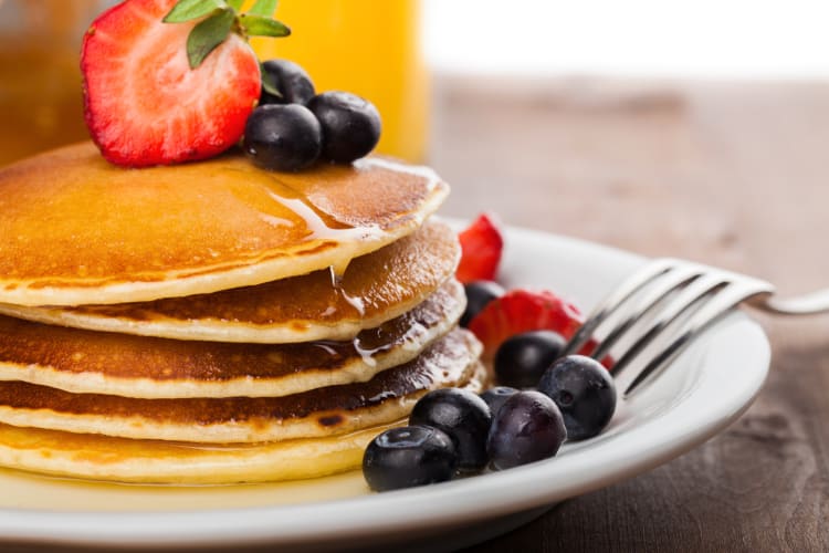 Stack of pancakes with strawberries, blueberries and syrup on top