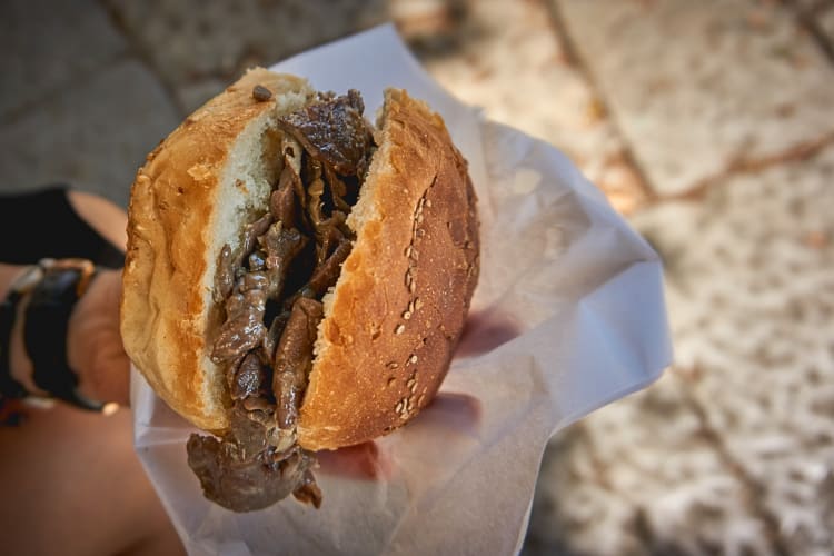 A person's hand holding pani câ mèusa inside of plastic sandwich paper