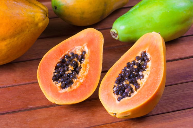 A halved papaya next to whole papayas