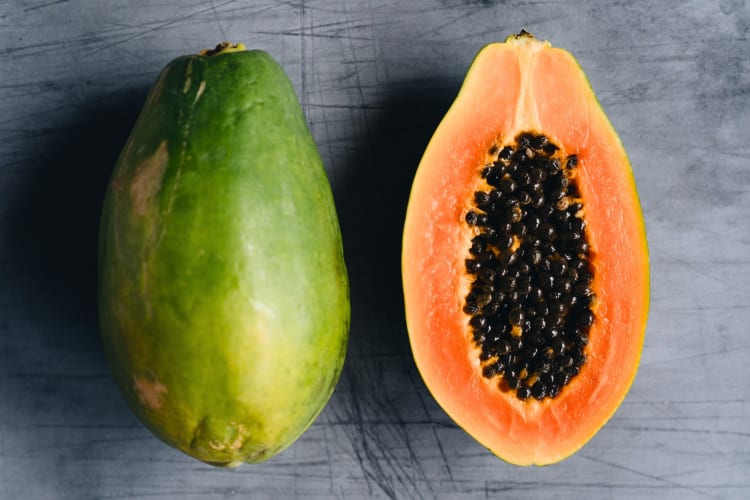 A whole papaya and a half papaya with orange flesh and black seeds