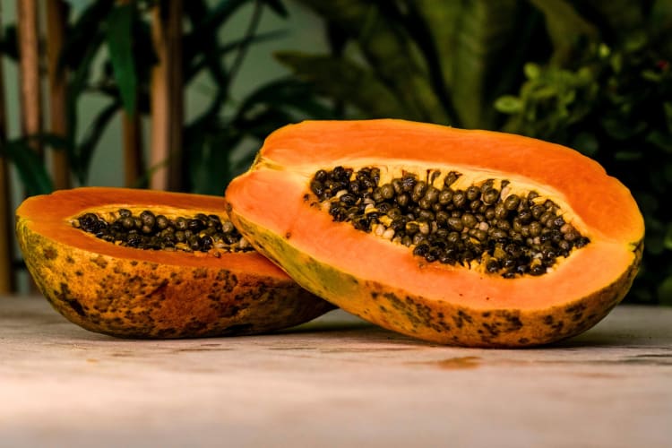 A papaya cut in half on a wooden surface with bamboo behind it