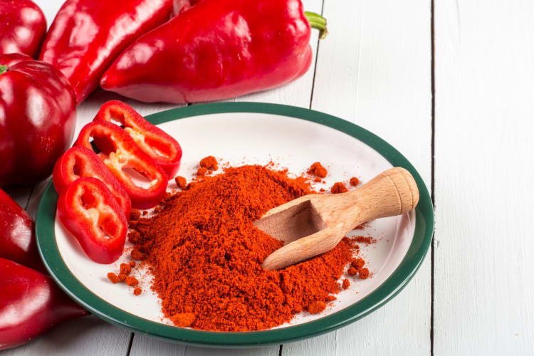 A bowl of paprika next to red peppers