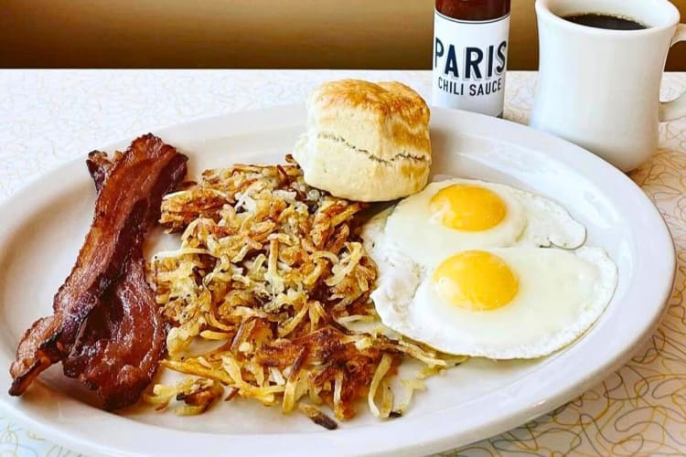 A breakfast meal with eggs, bacon, a hash brown and a biscuit, from a Paris Coffee Shop