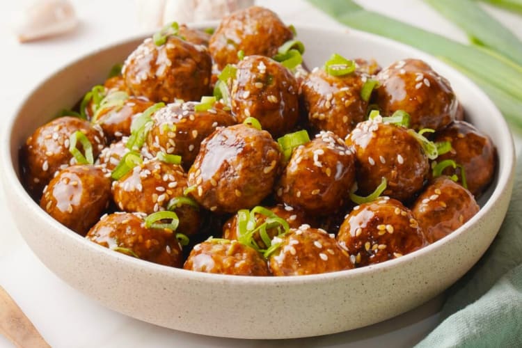 A bowl with meatballs garnished with green onions and sesame seeds