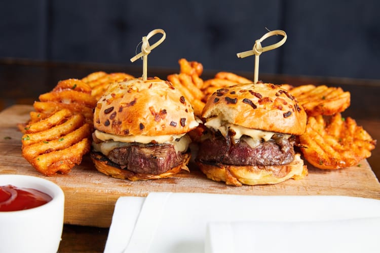 Two sliders with crinkle-cut fries and tomato sauce in the foreground