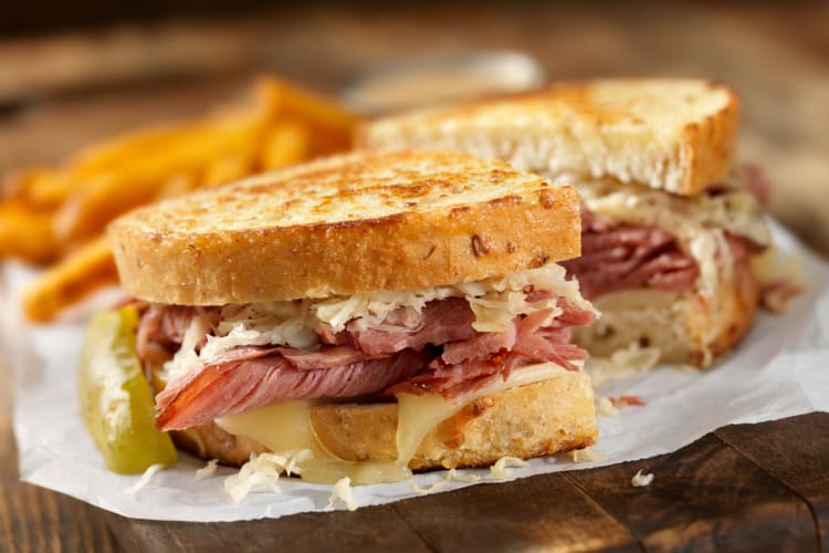 A Reuben on a plate next to pickles and fries