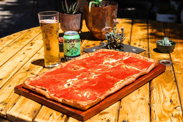 A rectangle pizza on a patio table next to beer and plants