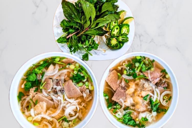 Two pho bowls with a plate of greens from Pho 24