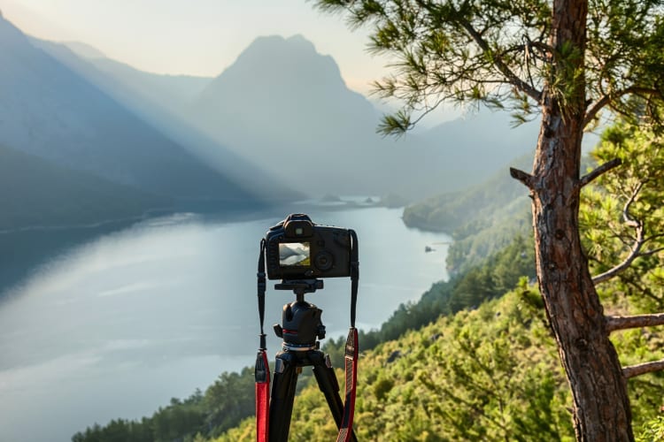 A camera set up on a tripod with mountains and a dam ahead of it