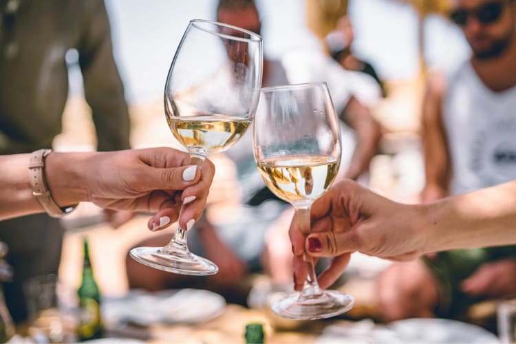 Two people cheers glasses of white wine in an outdoor setting