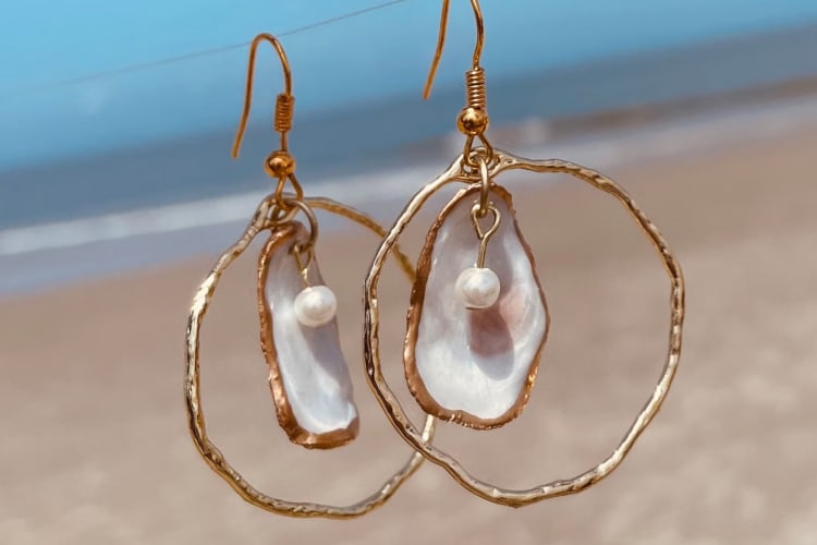 Seashell hoop earrings hanging on a wire with a beach in the background