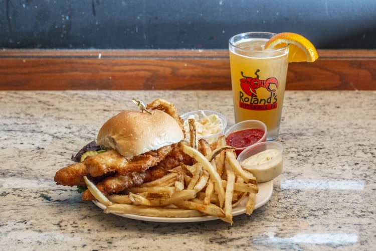 A fish burger with fries and a beer.