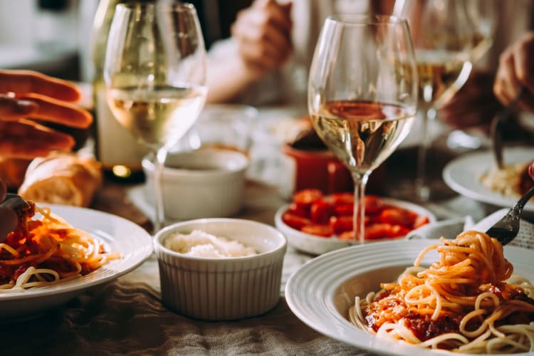 A close-up of 2 people eating dinner and drinking glasses of wine.