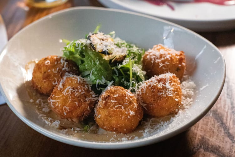 A bowl of arancini, garnished with greens and grated Parmesan.