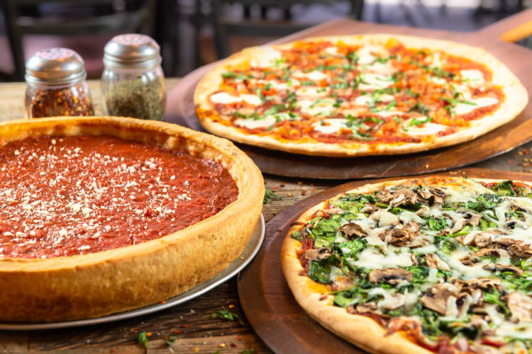 A deep dish pizza and two thin crust pizzas on a table