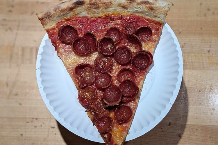 Slice of pepperoni pizza on a paper plate, from Pizza Supreme Being