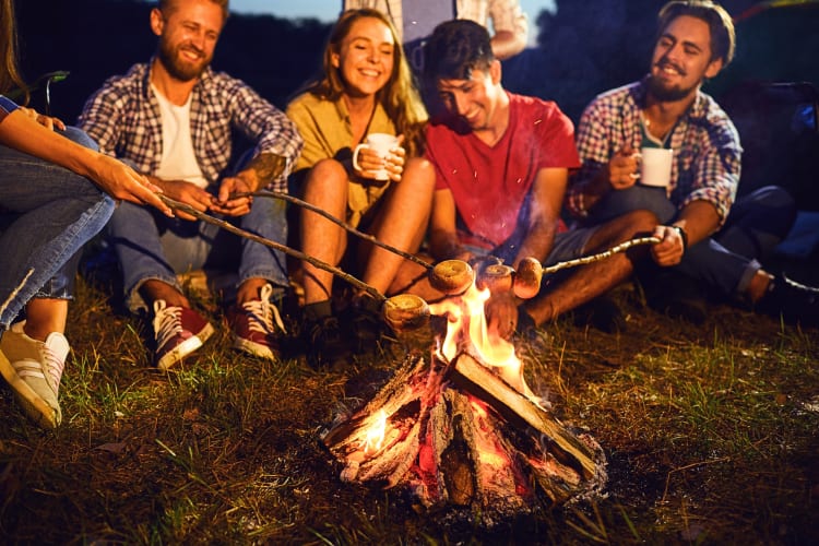Five friends roasting marshmallows over a fire during a camping adult birthday party idea