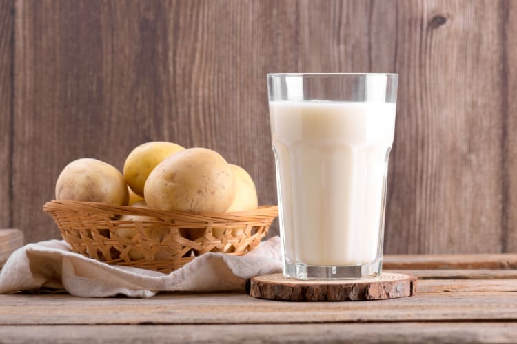 A glass of potato milk next to potatoes