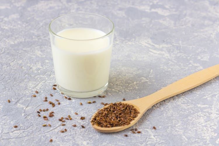 A glass of flax milk next to a wooden spoon with flax seeds