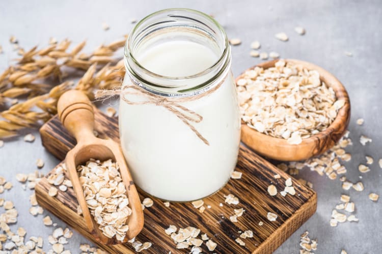 A jar with oat milk on a wooden board with oats