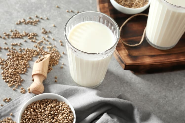 A glass of hemp milk next to a wooden board and hemp seeds